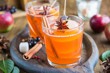 Autumn hot drink, spicy apple cider with apple slices in glasses on a wooden tray. American cuisine.