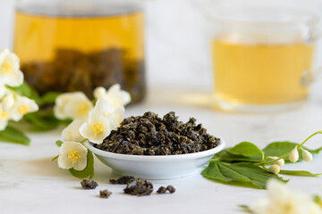 Chinese large leaf green tea with jasmine on white marble background, closeup. Dry leaves and brewed drink in teapot and cup