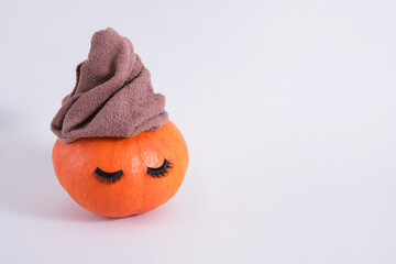 orange pumpkin with towel and false eyelashes on gray background