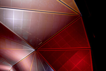 Modern architecture. Orange and red geometric metallic construction from triangular parts. Abstract background design in the dark.