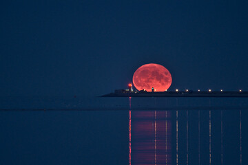 Beautiful view of rare summer full blue sturgeon Moon rising over Irish sky between Dun Laoghaire lighthouses on August 23, 2021 seen from Sandymount Beach, Dublin, Ireland. Huge Moon