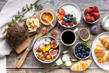 A table for a healthy breakfast with rye whole-grain bread, butter, granola, fresh berries, honey, porridge and croissants . Top view.
