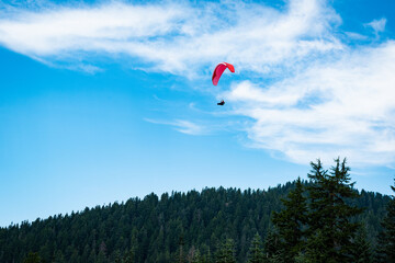 Photo of a distant red parasailer or paraglider flying over the Grouse Mountain area.