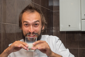 A man with a beard in a white shirt soaked and smeared his moustache with milk