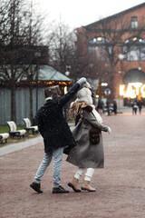 Obraz na płótnie Canvas Joyful young couple travel on Christmas enjoy walking outdoors spinning and dancing in empty old town. Happy lovers have fun outside on street in snow dressed in warm clothes during vacation together