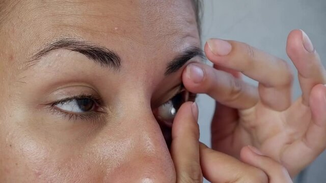 The brunette puts on contact lenses on her eye, holding her finger. Treating eye conditions such as myopia or myopia, astigmatism, or cosmetic lenses. Improvement and correction of vision.