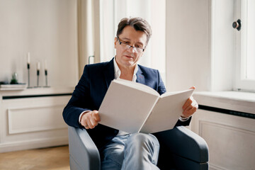 The lawyer is a successful stylish man who holds the legislation of the country in his hands. The lawyer is an adult man with gray hair, sitting in a business suit and thinking. 