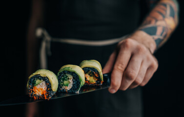 Unrecognizable man chef with a tattoo on his arm holds sushi rolls on a knife.