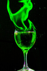Taça de vidro com borda quebrada cheia com liquido verde e chama de fogo de cor verde. 