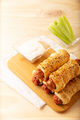 delicious snack of sausages wrapped in puff pastry with sesame seeds accompanied by cherry celery sticks and sauce. Served on wooden board