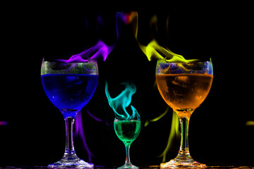 Taças de cristal cheias com bebida de cor azul, verde e cor laranja com bordas quebradas e labaredas de fogo coloridas.