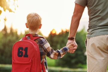 Little son schoolboy with backpack holding hand of father dad while going to first grade in school