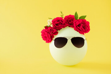 Creative arrangement of balloon with decoration of red roses and leaves and black sunglasses against bright yellow background. Minimal end of summer concept. Copy space.