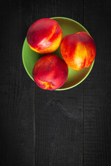 Three red ripe nectarine hybrids in their ripening season lie on green plate or on a dark vintage...