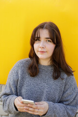 Fototapeta premium Woman using mobile phone next to the yellow background. Social media screen. Clubhouse the voice-only social media app. Clubhouse, a social platform built around drop-in audio chat. Using social app 
