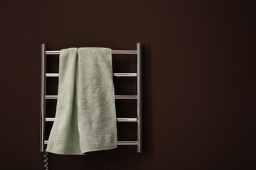 Modern heated towel rail with warm soft towel on brown wall. Space for text