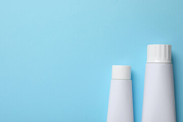 Blank tubes of toothpaste on light blue background, flat lay. Space for text