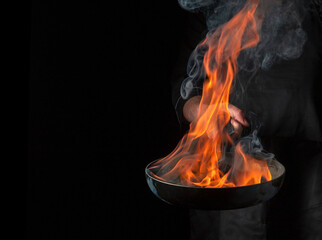 Professional chef cooking food in pan with fire flame on black background. Restaurant and hotel...