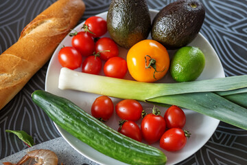 Fresh vegetables on a white plate, avocado, shallots, tomatoes, cucumber. For the day of vegetarianism