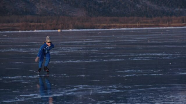 The girl train on ice speed skating. The child skates in the winter in blue sportswear suit, sport glasses. Children speed skating sport. Outdoor slow motion. Snow capped mountains, beautiful ice.