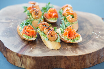 Bruschetta with avocado and salmon, shrimp sandwich on a buffet plate on a wooden stand