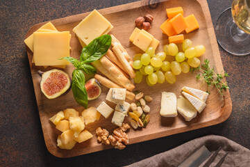 Cheese platter with grapes, nuts, figs on a brown background. Top view. Close up. Festive gourmet snack.