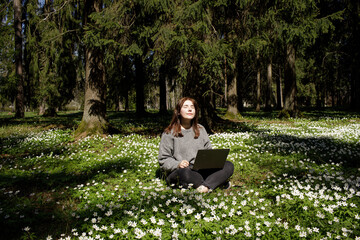 Young woman laying in green grass next to the laptop. People fatigue from work. Sleeping and...