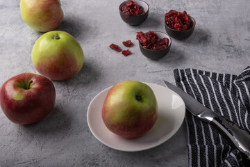 Delicious red apples, a knife prepared for cutting an apple, small bowls with dried cranberries, on a beautiful concrete background.