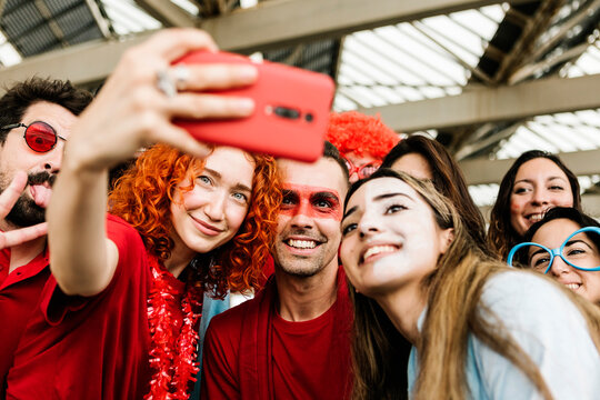 Multiethnic group of young people taking selfie out of the stadium - Football fans having fun together - Focus on painted face man