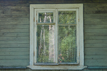 Old white wooden window in an old wooden rustic green house with green plank walls
