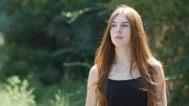 Portrait of a young girl smoking a vape. IQOS. Woman puffs on a vape pen. Blowing smoke out of your mouth is delicious.