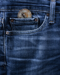 plano cercano de un bitcoin en el bolsillo pequeño delantero de un vaquero azul.