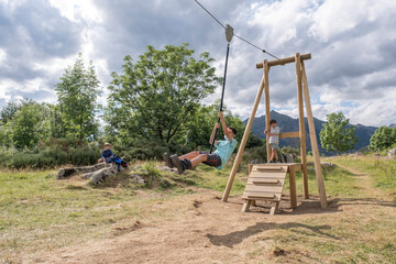 boy wearing a face mask jumps off a playground zip line in summer camp as others look at him