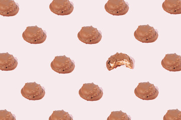 Fototapeta premium Chocolate cookies arranged in a pattern in which one cookie is bitten on a pink background. Party sweet food concept.