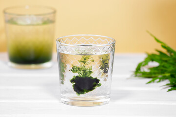 Green Chlorophyll drink in glass with water drops on white table, Orange Background. Antioxidant food and drinks.
