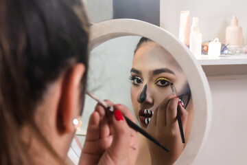Beautiful girl doing her skull teeth makeup for Halloween with her little mirror in her room.