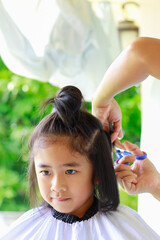 Obraz premium Mother uses scissors to cut her daughter's hair outside the house. Beauty salon concept, new normal covid-19.