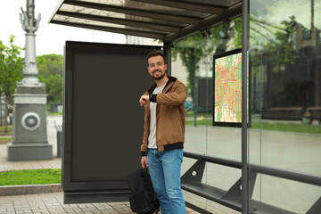 Young man with backpack waiting for public transport at bus stop