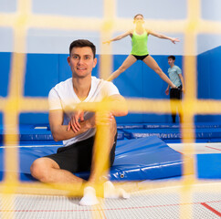 Portrait of satisfied athletic man relaxing after workout on trampolines, view through yellow safety net