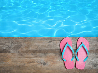 Pair of flip flops on wooden deck near swimming pool, top view