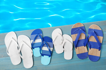 Naklejka premium Pairs of flip flops on wooden deck near swimming pool, flat lay