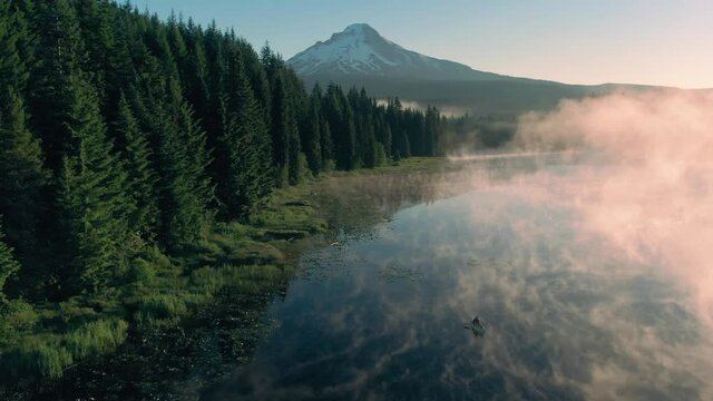 Aerial: Canoe rowing on Trillium Lake, mist, pine forest and Mt Hood at sunrise, Oregon, USA