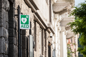 Electric defibrillator logo on a sign in an urban environment, abiding by European standards, indicating nearby presence of AED device, an obligation to deal with cardiac diseases and heart attacks - obrazy, fototapety, plakaty