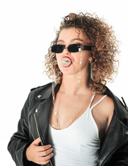 Stylish curly hair woman in sunglasses and leather jacket  
inflates the gum on white background