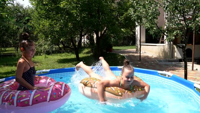 Happy girls swim in donut pool floats in swimming bath on sunny summer day, pool