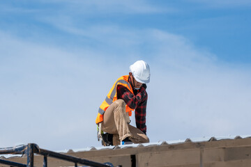 Roofer worker in protective uniform wear and gloves working installing metal sheet on top of the new roof at construction site.
