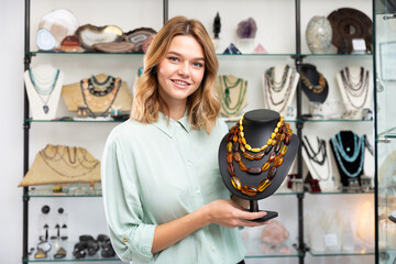 Portrait of cheerful female shop assistant demonstrating amber necklace