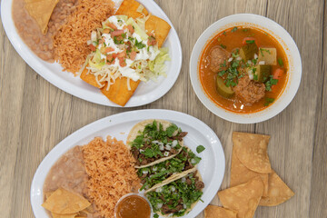 Variety of plates on the table with the carne asada tacos, enchiladas, and albondigas soup to choose from