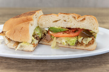 Fototapeta premium Hearty carnitas pork torta sandwich cut in half to show all the chopped peppers and vegetables with the meat and bread bun