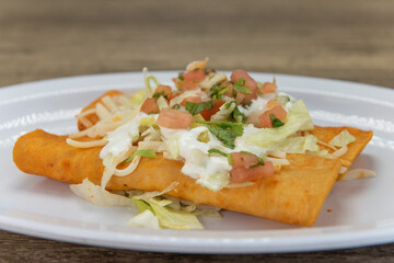 Hearty appetizer of two enchiladas covered in sour cream, pico de gallo, and cheese
